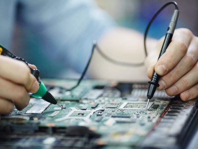 Closeup shot of male hands testing electric current voltage in circuit board of disassembled laptop using multimeter tool on table in maintenance shop
