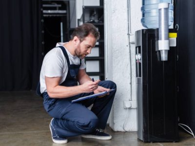 side view of male repairman writing in clipboard during checking of broken water cooler