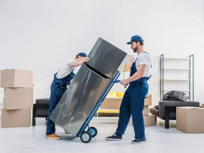 two-movers-in-uniform-using-hand-truck-while-transporting-refrigerator-in-apartment-1024x684